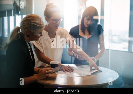 Three businesswomen discussing over documents on table. Female colleagues having a standing meeting around table in office. Stock Photo