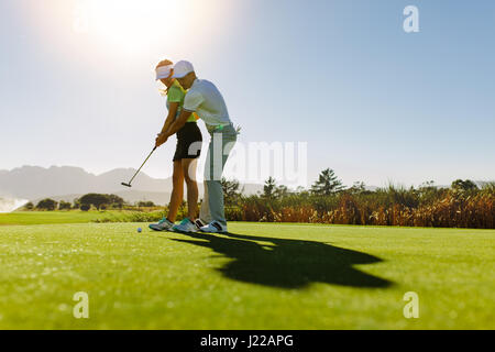 Man teaching woman to play golf while standing on field. Personal trainer giving lesson on golf course. Stock Photo