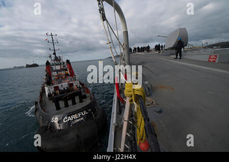 170417-N-ZE250-034   PLYMOUTH, United Kingdom (April 17, 2017) - A tug boat guides USS Carney (DDG 64) into position to moor to a buoy in Plymouth, United Kingdom while participating in Flag Officer Sea Training (FOST) April 17, 2017. Carney, an Arleigh Burke-class guided-missile destroyer, forward-deployed to Rota, Spain, is conducting its third patrol in the U.S. 6th Fleet area of operations in support of U.S. national security interests in Europe. (U.S. Navy photo by Mass Communication Specialist 3rd Class Weston Jones/Released) Stock Photo