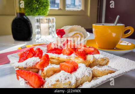 Poffertjes (Dutch mini pancakes) with strawberries, powdered sugar, and whipped cream, with a side of coffee at a Dutch cafe. Stock Photo