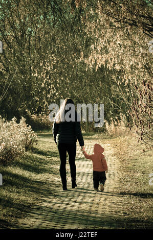 Mom walking toddler son on a trail in the woods Stock Photo