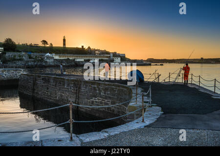 Anglers are treated to a golden sunrise on the Waterfront Harbour as the sun rises behind Smeatons Tower in Plymouth, Devon. Stock Photo