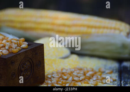 Close-up shoot of handmade embossed chest full of corn grains; bokeh of corn cob, corn flour and beans. Stock Photo