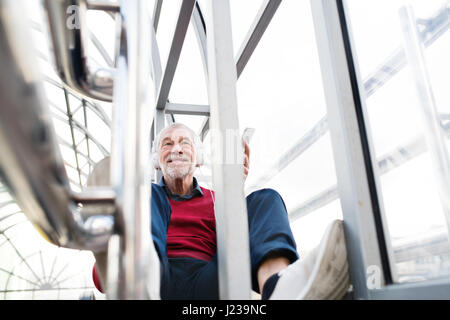 Senior man with smartphone and headphones sitting in passage. Stock Photo