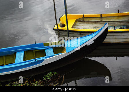 Two Portuguese blue and yellow row boats anchored in a calm river shore Stock Photo