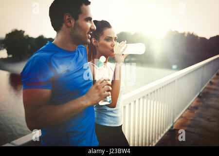 Couple drinks water to replenish energy and to hydrate after jogging Stock Photo