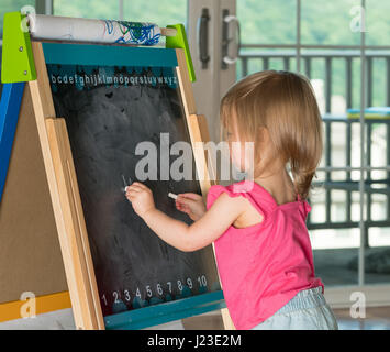 Young child learning to write and writing with chalk on a blackboard Stock Photo