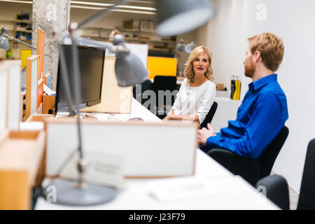 Coworkers communicating while sitting at their desk in a nice office Stock Photo