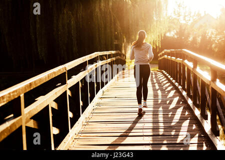 Beautiful female jogger running during sunset across bridge