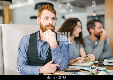 Pensive young leader of creative team and his co-workers on background Stock Photo