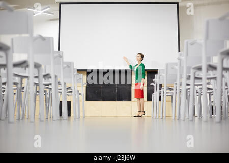 Young teacher pointing at whiteboard while explaining new topic Stock Photo