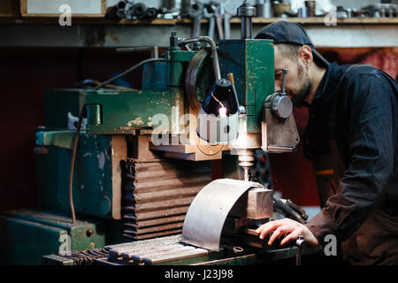 Portrait of man in workers uniform using drilling unit to make metal parts Stock Photo