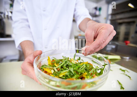 Chef adding pinch of salt into vegetarian salad Stock Photo