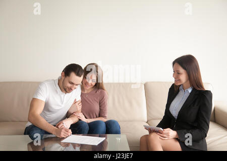 Young man signing papers sitting next to wife and realtor Stock Photo