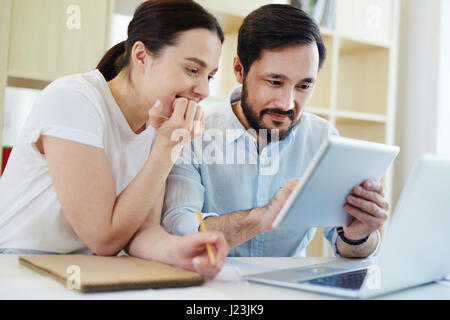 Portrait of smiling man and young woman using modern digital devices at desk Stock Photo