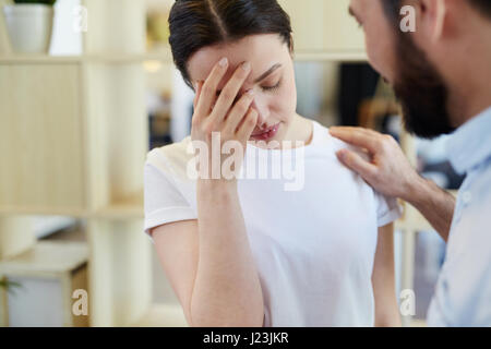 Portrait of troubled young woman crying and covering face with man trying to console her Stock Photo