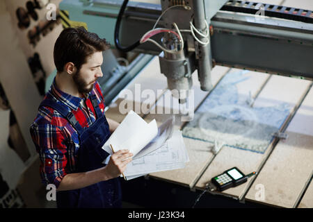 Engineer with papers standing by milling-machine in workshop Stock Photo