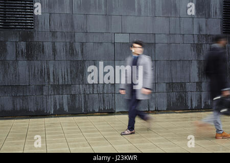 Hurrying men walking down trottoire along black wall of modern building Stock Photo