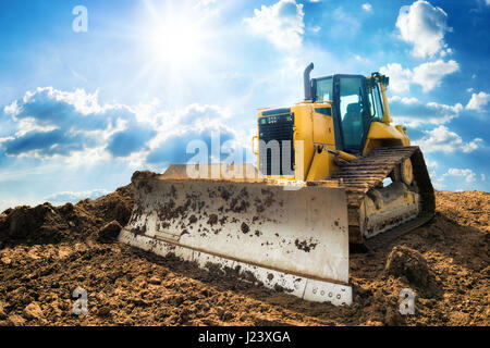 Yellow excavator on new construction site, with the bright sun and nice blue sky in the background Stock Photo