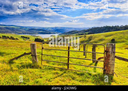 Grazing hill sides surrounding Lake Lyell on Coxs river in Australian Blue Mountains country. Entry gate to the green pasture under warm sun light. Stock Photo