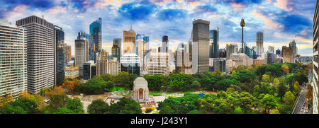 Wide panorama over Hyde Park south and north towards Sydney city CBD towers at sunset when bright sunlight reflects from sky clouds. Stock Photo
