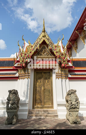 Two statues in front of a decorated door and gate at the Wat Pho (Po) temple complex in Bangkok, Thailand. Stock Photo
