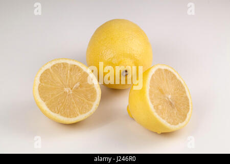 Two ripe lemons on of which is cut into halves placed on a white background Stock Photo