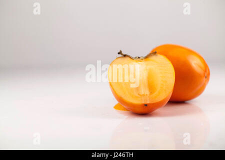 Two persimmons or kaki fruits on a white background. One fruit cut into two