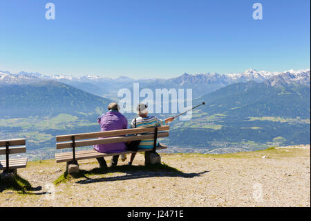 Two senior men sitting on a wooden bench admiring the panoramic view of the mountains from Hafelekarspitze, Tirol, Austria Stock Photo