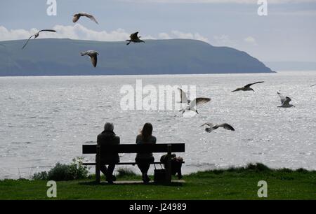 Woolacombe Beach, Devon, UK. 24th Apr, 2017. Two people sit on a bench admiring the view with gulls flying all around them as sunny spells bring people out to this popular beach. Credit: DTNews/Alamy Live News Stock Photo