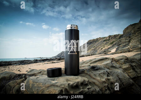 Thermos flask sitting on rocks by the sea Stock Photo