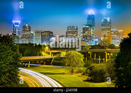 Traffic light trails in Charlotte, North Carolina. The city skyline glows on a foggy night.