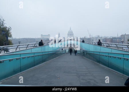 Commuters walking to work across Millennium Bridge, London, UK looking towards St Paul's Cathedral, shrouded in fog Stock Photo