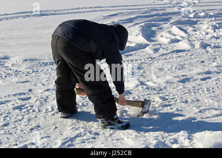 Chopping at an Old Ice Fishing Hole with an Axe. Stock Photo