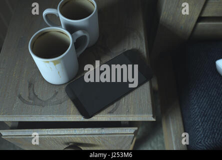 A real life concept scene showing a bed side table with dirty coffee mugs and a generic smartphone at night - 3D Render Stock Photo