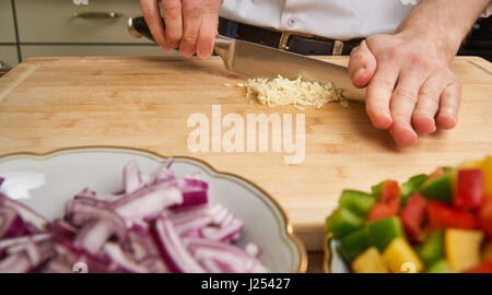 Man's hands cutting fresh garlic in the kitchen, preparing a meal for lunch. Paprika and onions in the foreground. Stock Photo