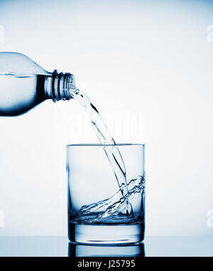 Water pouring into a wide glass from a bottle tinted in blue Stock Photo