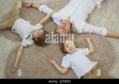 Top view of young father with cute little sons lying on floor Stock Photo
