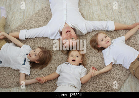 Top view of young father with three cute little sons lying on floor Stock Photo