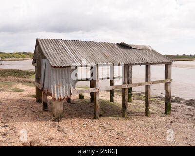 an old and abandoned sea shack shed decaying and rotting in the sun as seen from the side and back at the beach and seafront made of wooden and metal Stock Photo