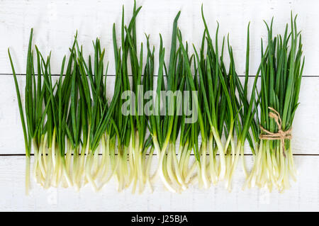 Young feathers (leaves) of a green onion on a white wooden background, collected in a bundle and scattered. The top view. The first spring greens. Ing Stock Photo