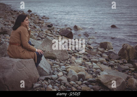 Side view of woman sitting on rock at beach Stock Photo