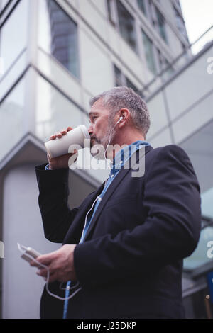 Businessman using phone while drinking coffee against building Stock Photo