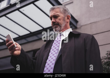 Low angle view of businessman using smart phone while standing against building Stock Photo