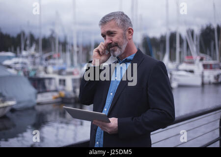Businessman using smart phone while holding tablet PC by harbor Stock Photo