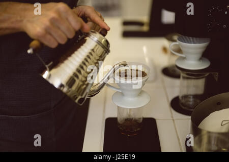 Barista hands pouring hot water through funnel in coffee shop Stock Photo