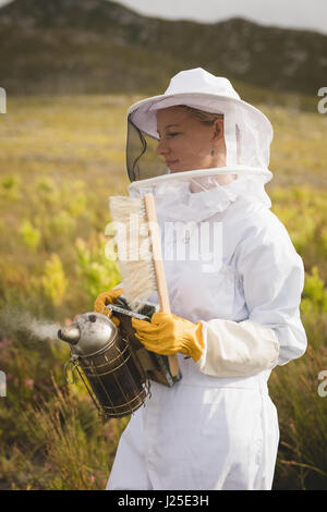 Female beekeeper holding bee smoker and brush on farm Stock Photo