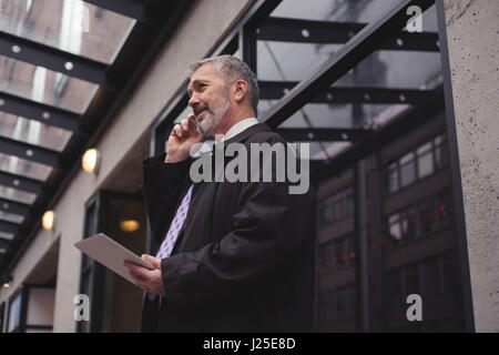 Businessman talking on smart phone while standing against building in city Stock Photo