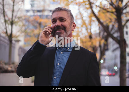Happy businessman using smart phone during autumn in city Stock Photo