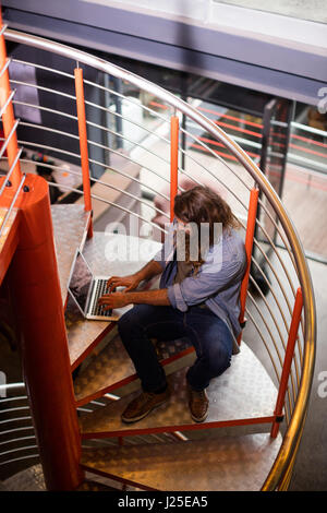 Sound engineer using laptop on stairs in office Stock Photo